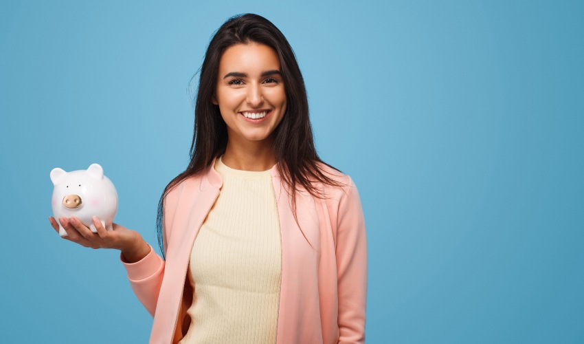 woman in acardigan holds a piggy bank against a wall to represent affordable dental care