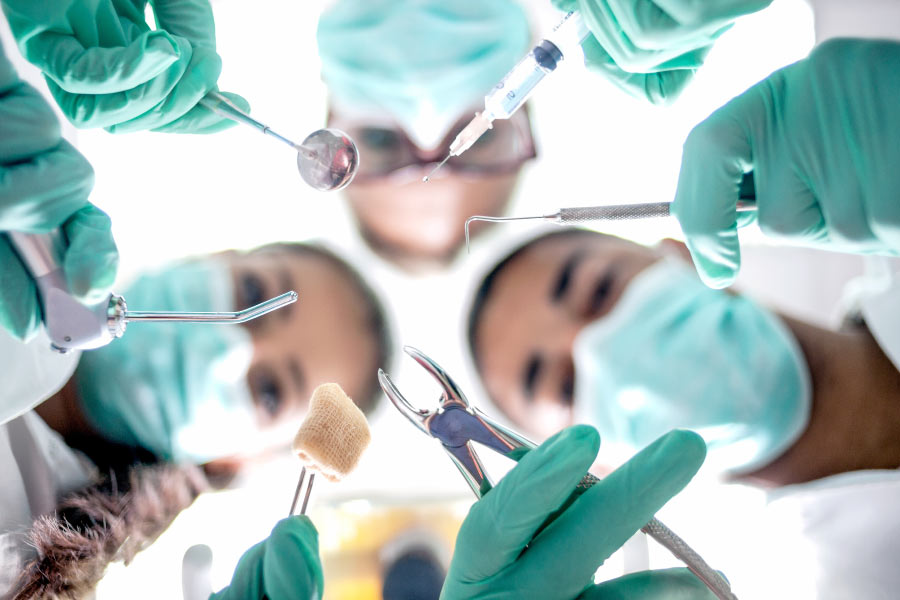 Upward looking at masked faces of technicians holding tools used for oral surgery