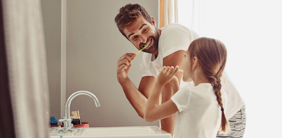Father and young daughter brushing their teeth together at the bathroom sink.