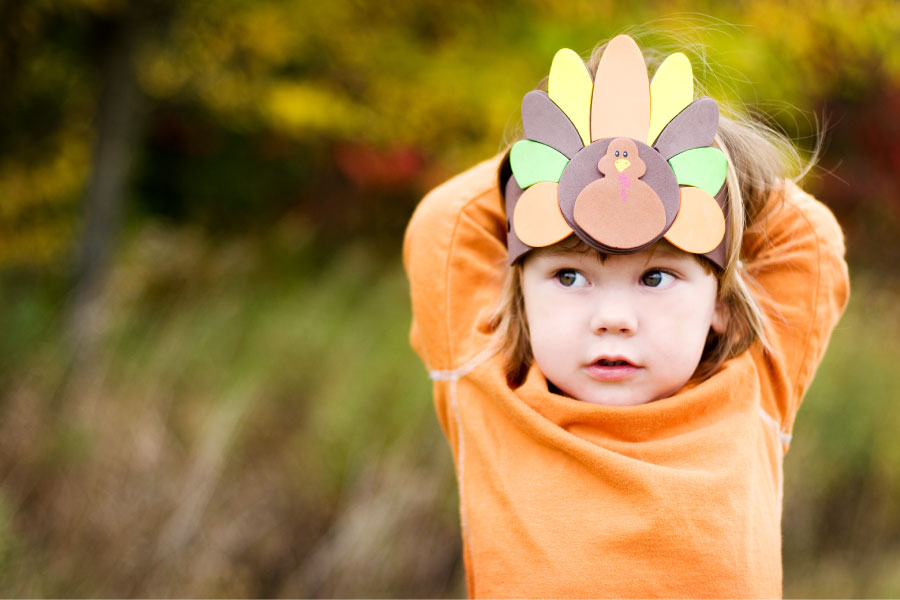 Young child in an orange shirt wearing a turkey hat for Thanksgiving.