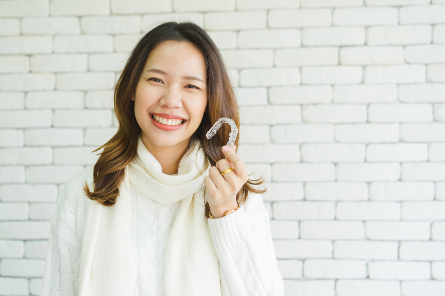 Smiling woman holding a clear aligner.